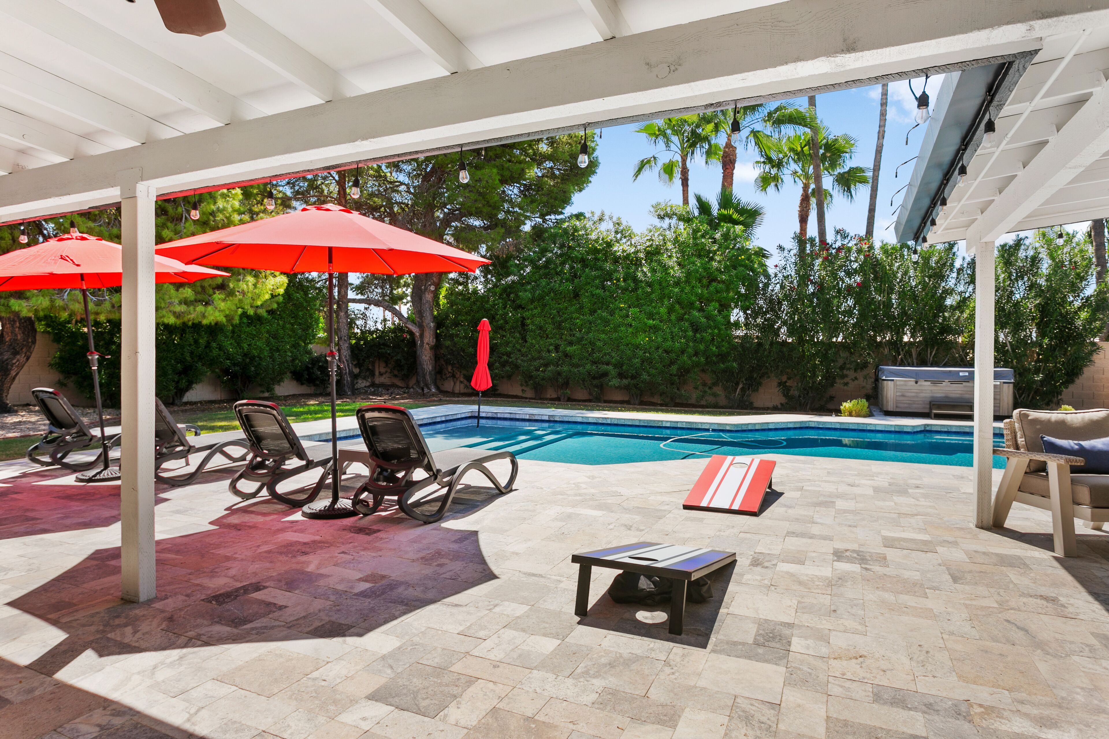A covered outdoor area with a pool, lounge chairs, and umbrellas.