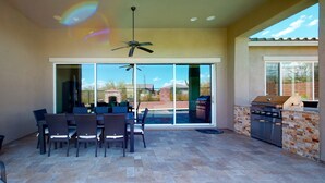 An outdoor patio with a dining table and chairs, a ceiling fan, and a barbecue grill.