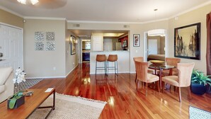 Un vaste espace de vie doté d’un plancher en bois, d’une table à manger avec des chaises, d’une cuisine à l’arrière-plan et d’un ventilateur de plafond.