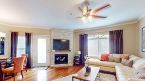 Un salon avec une cheminée, un ventilateur de plafond, un téléviseur fixé au mur et un canapé.