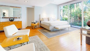 Ein modernes Schlafzimmer mit einem großen Bett, einer Sitzecke mit Couchtisch, einem Schminktisch und einem großen Fenster mit Blick auf Grünflächen.