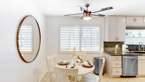 A kitchen with white cabinets, a dishwasher, and a dining area with a table set for two. - Gorgeous Palm Desert Oasis with Backyard Paradise, Pool, Spa & Private Casita (Palm Desert)