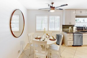 A kitchen with white cabinets, a dishwasher, and a dining area with a table set for two. - Gorgeous Palm Desert Oasis with Backyard Paradise, Pool, Spa & Private Casita (Palm Desert)