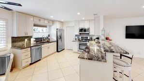 A modern kitchen with stainless steel appliances, a marble countertop, and a flat-screen TV mounted on the wall. - Gorgeous Palm Desert Oasis with Backyard Paradise, Pool, Spa & Private Casita (Palm Desert)