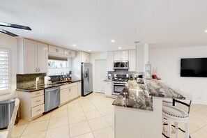 A modern kitchen with stainless steel appliances, a marble countertop, and a flat-screen TV mounted on the wall. - Gorgeous Palm Desert Oasis with Backyard Paradise, Pool, Spa & Private Casita (Palm Desert)