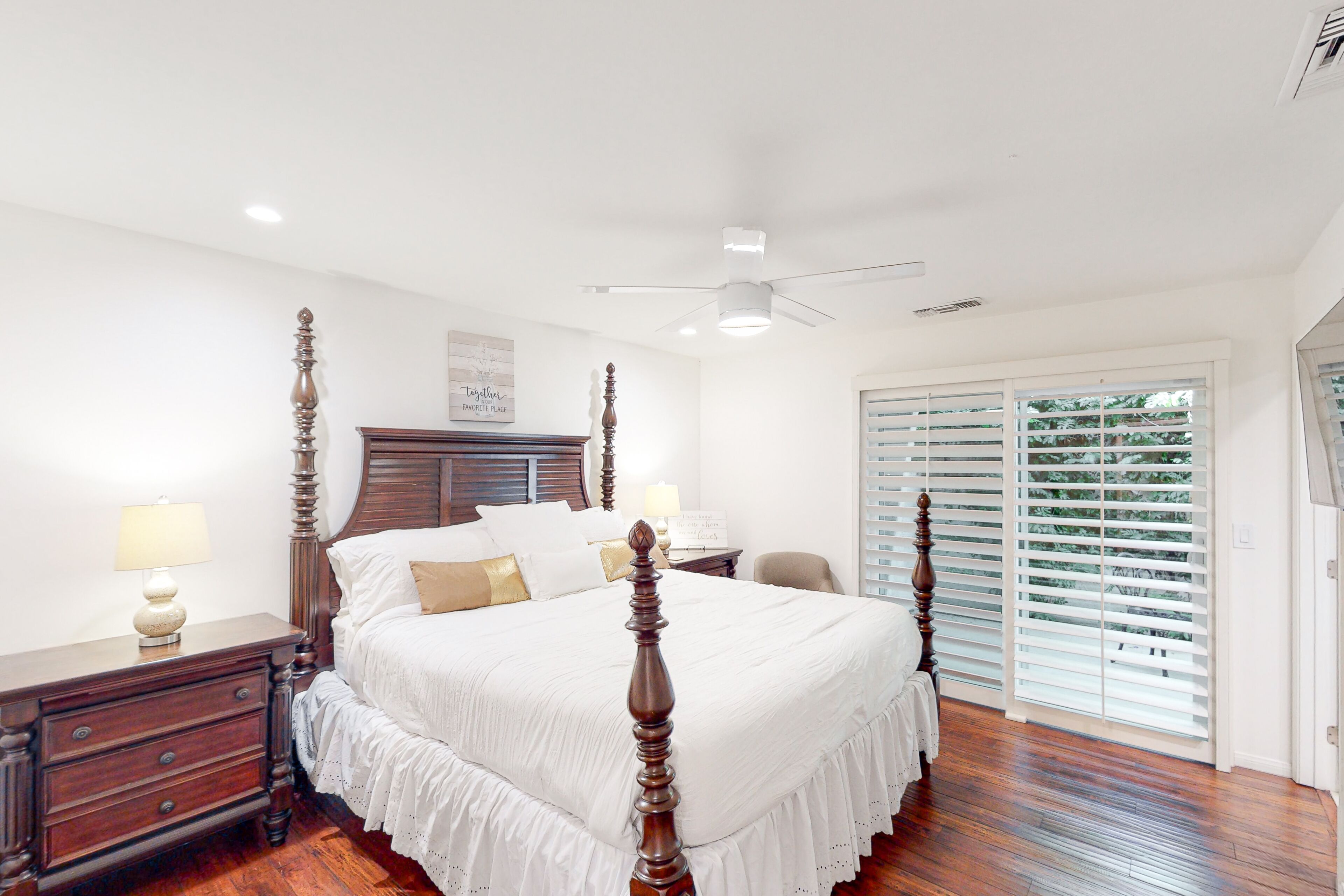 A spacious bedroom with a large bed, wooden headboard, and a ceiling fan.