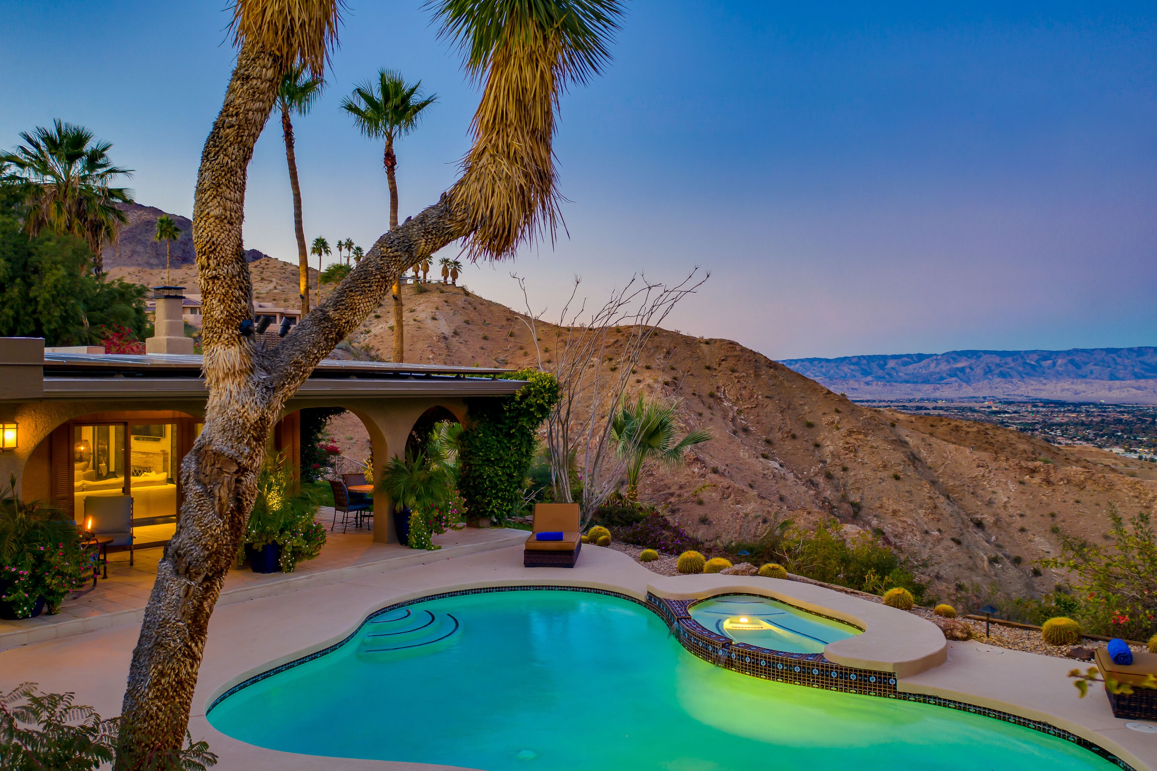 A pool area with two distinct sections, surrounded by palm trees and a view of a mountainous landscape.