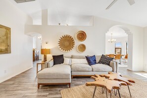 Un salon moderne avec un canapé d’angle, des œuvres d’art décoratives au mur et une table basse en bois.