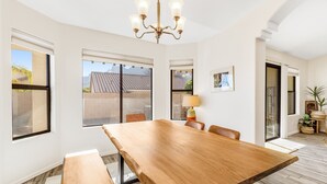 Een ruime eethoek met een grote houten tafel, comfortabele zitplaatsen en een kroonluchter.
