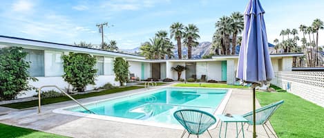 A swimming pool with a diving board, surrounded by a well-maintained lawn and a building with a white exterior.