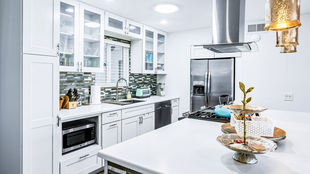 Une cuisine moderne avec des meubles blancs, une hotte en acier inoxydable et un îlot central agrémenté d’une plante décorative.