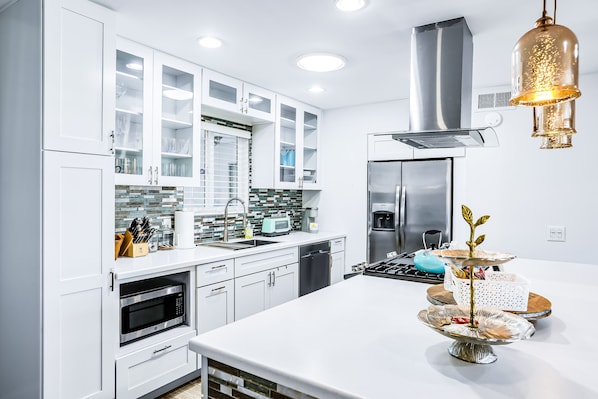 A modern kitchen with white cabinetry, a stainless steel range hood, and a central island with a decorative plant.