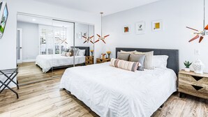 Une chambre à coucher moderne avec un grand lit, un miroir, un ventilateur de plafond et une petite table de chevet avec une lampe.