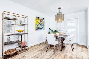 A dining area with a wooden floor, white chairs, a glass-top table, and a decorative metal shelf with various items.