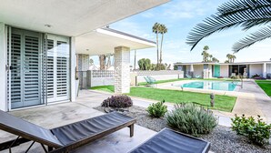 Une terrasse extérieure moderne, dotée de chaises longues, d’une piscine et d’une pelouse bien entretenue.