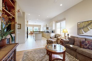 A spacious living area with a sofa, a coffee table, and a dining table. There is a kitchen in the background with cabinets and a window. - PGA west home with pool, gas grill spa and washer/dryer (La Quinta)