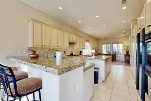 A spacious kitchen with granite countertops, white cabinetry, and a central island with bar stools. - PGA west home with pool, gas grill spa and washer/dryer (La Quinta)