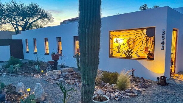 Een modern gebouw met een groot raam dat een woestijnlandschap toont. Langs de zijkant van het gebouw bevinden zich meerdere ramen, en een cactus staat opvallend op de voorgrond.