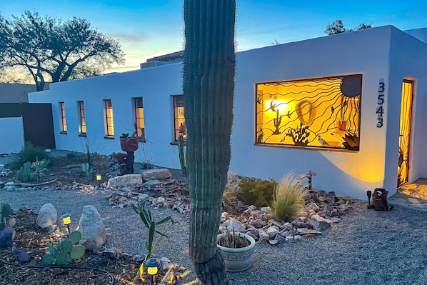 A modern building with a large window displaying a desert landscape. There are multiple windows along the side of the building, and a cactus is prominently featured in the foreground. - Dog-friendly desert oasis with private hot tub in Tucson's mid-town (Tucson)
