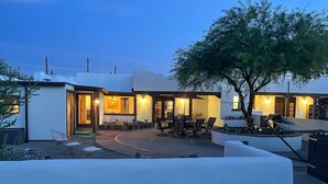 Een modern huis met een terras, zitplaatsen buiten en een boom.