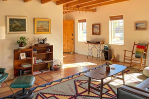 A cozy living room with a sofa, a dining table, a bookshelf, and a kitchen area with a wooden door. - Dog-friendly desert oasis with private hot tub in Tucson's mid-town (Tucson)