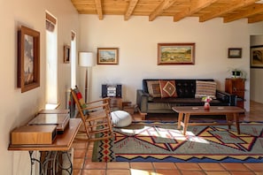 Una sala de estar con sofá, mesa de centro, mecedora de madera y alfombra estampada.