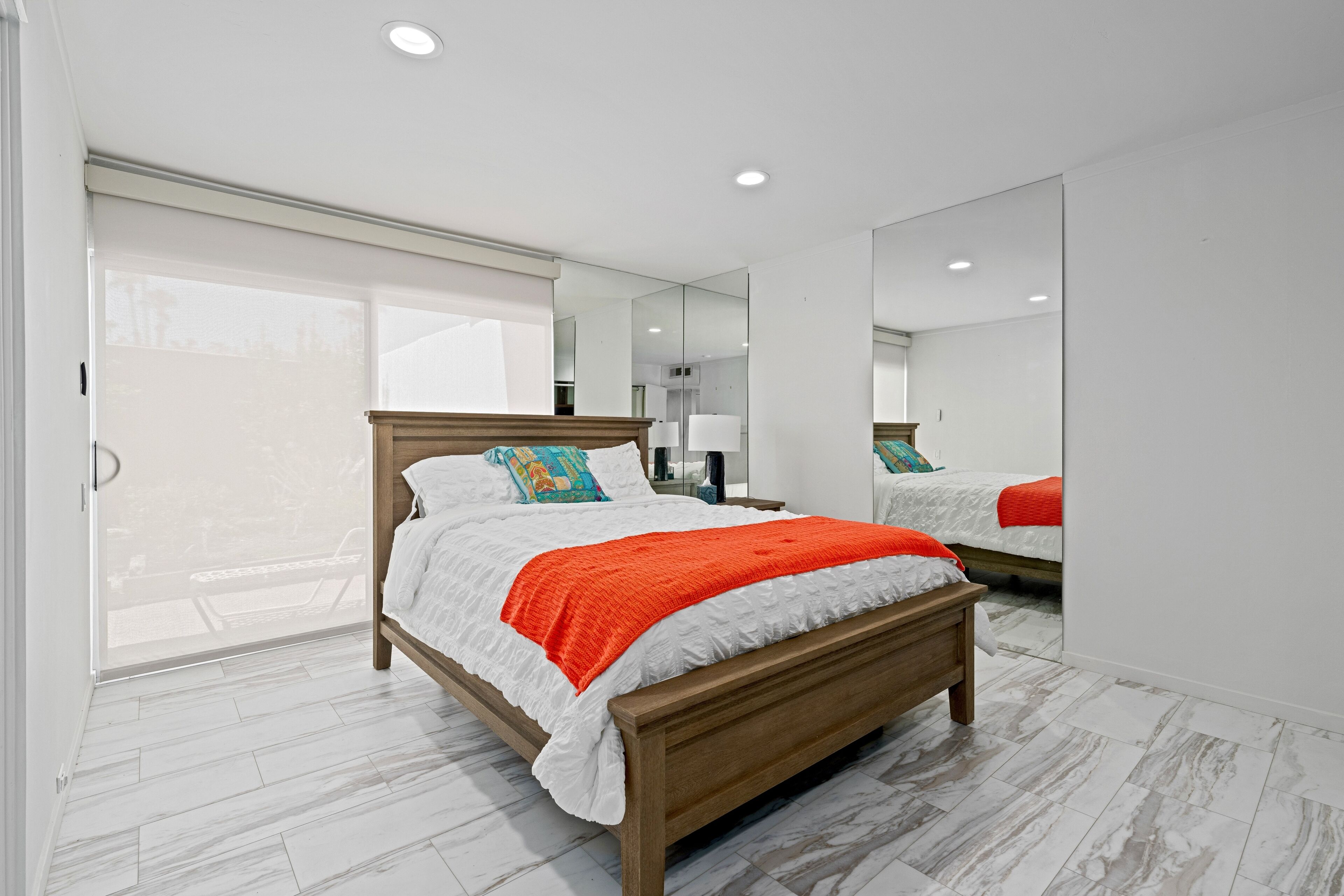 Quarto moderno com cama de madeira, roupa de cama branca e manta vermelha.
