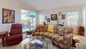 A living room with a red armchair, a patterned sofa, a glass coffee table, and a ceiling fan. - Dog-friendly desert home with mountain views, enclosed yard, grill, W/D, and AC (Oro Valley)
