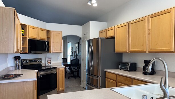 A modern kitchen with wooden cabinets, stainless steel appliances, a built-in oven, and a large sink. - Dog-friendly desert home with mountain views, enclosed yard, grill, W/D, and AC (Oro Valley)