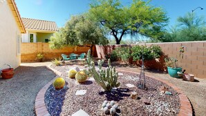 A garden with cacti and a tree, a brick wall, and a building with a tiled roof. - Dog-friendly desert home with mountain views, enclosed yard, grill, W/D, and AC (Oro Valley)