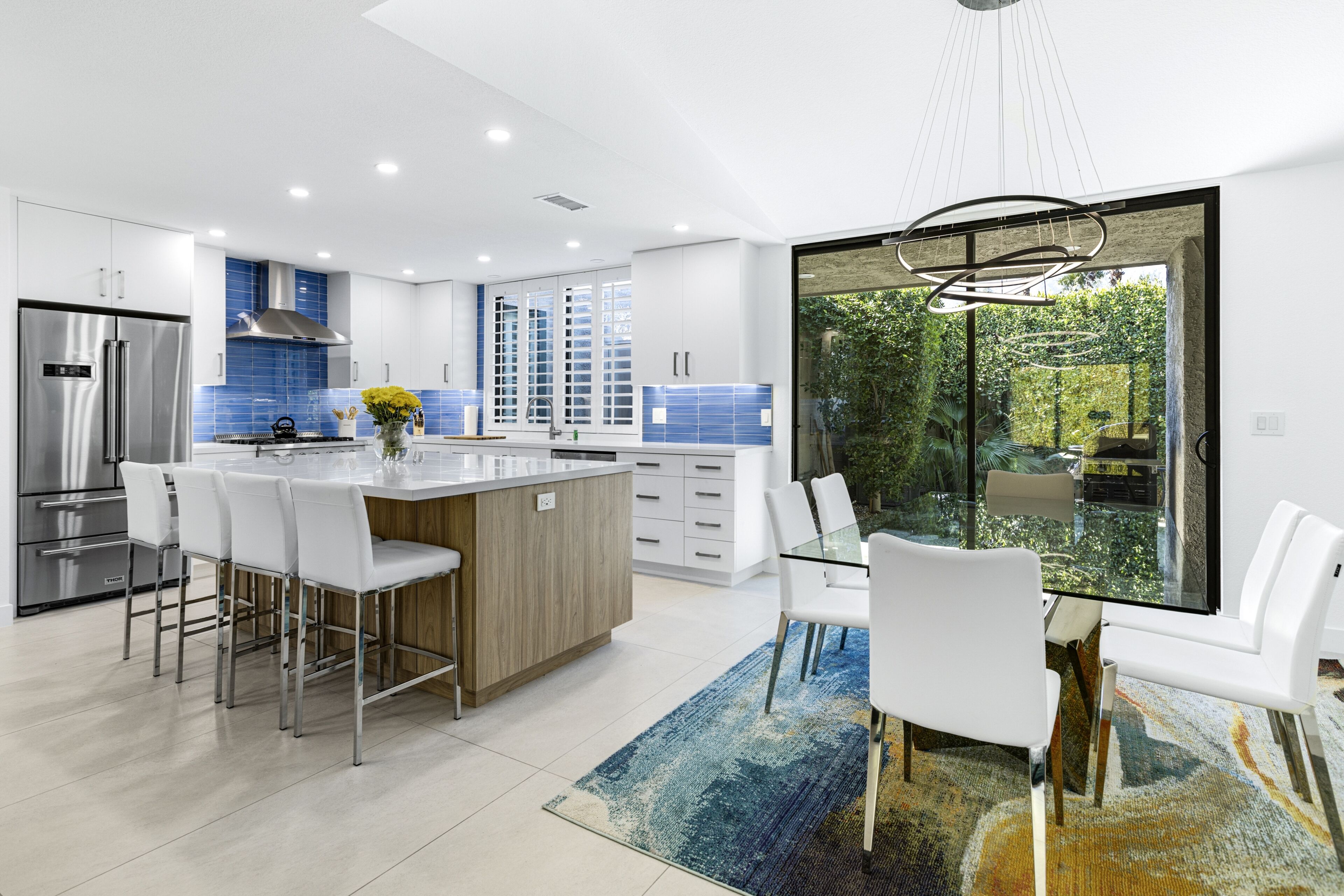 A modern kitchen with a central island, stainless steel appliances, and a dining area with white chairs.