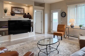 A living room with a flat-screen TV, leather sofas, a glass coffee table, and a fireplace with decorative items. - 2nd-floor condo with sunset, mtn, & valley views, hot tub, pool, gym, balcony (Oro Valley)
