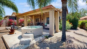 Een overdekt terras buiten, met een hottub, palmbomen en een huis met een pannendak.
