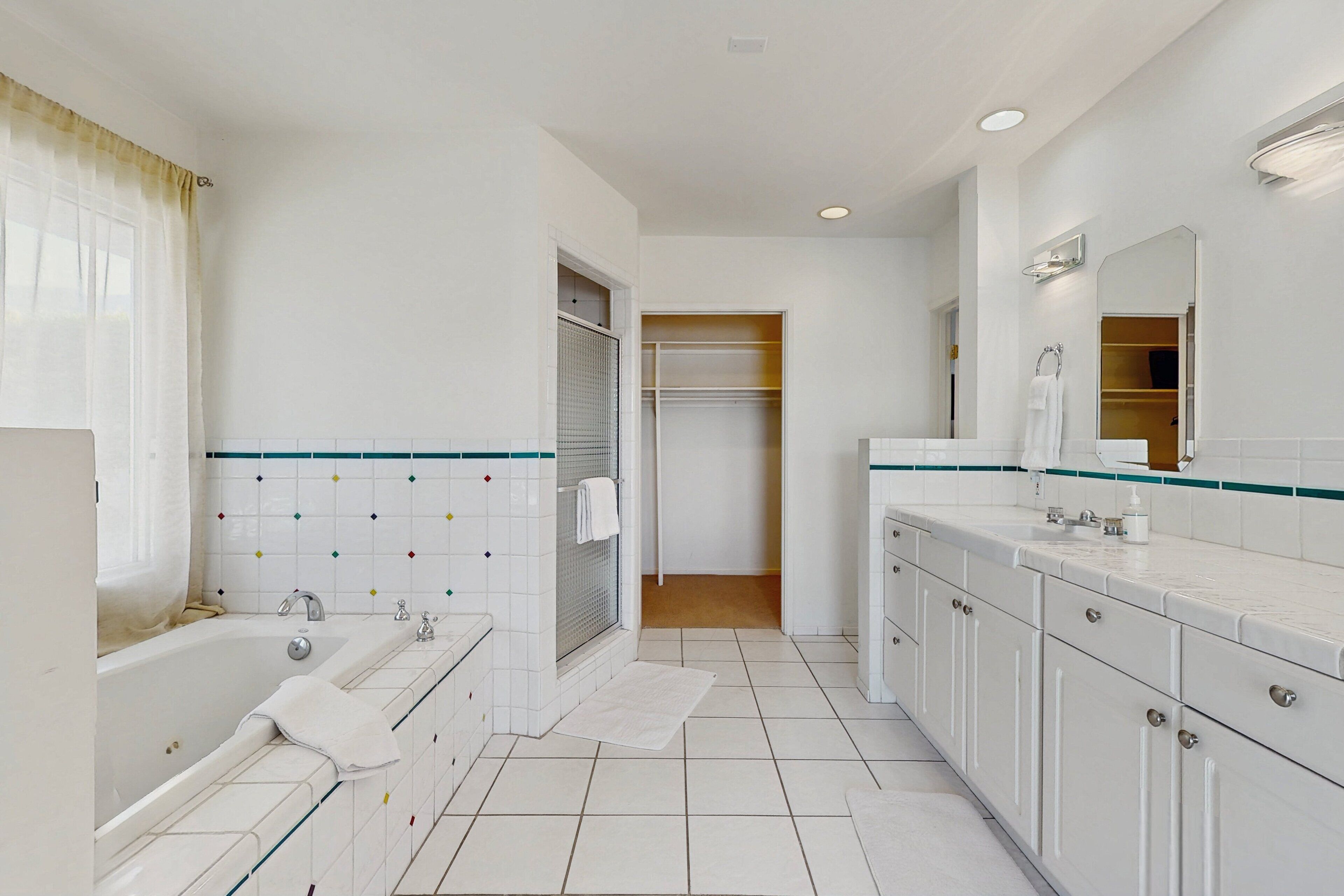 A modern bathroom with a bathtub, a shower, a vanity with a mirror, and a walk-in closet.