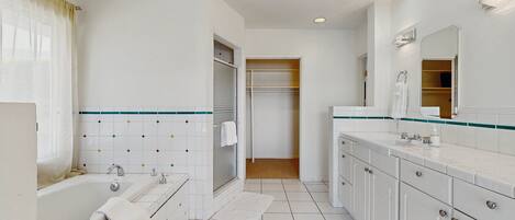 A modern bathroom with a bathtub, a shower, a vanity with a mirror, and a walk-in closet.