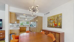 Una cocina moderna con armarios de madera, una isla central y un comedor con una mesa redonda y sillas naranjas.