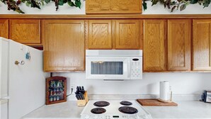 A kitchen with wooden cabinets, a white microwave, a stove, and a spice rack.