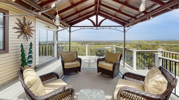 A covered outdoor patio with wicker furniture, a table, and a view of the landscape.