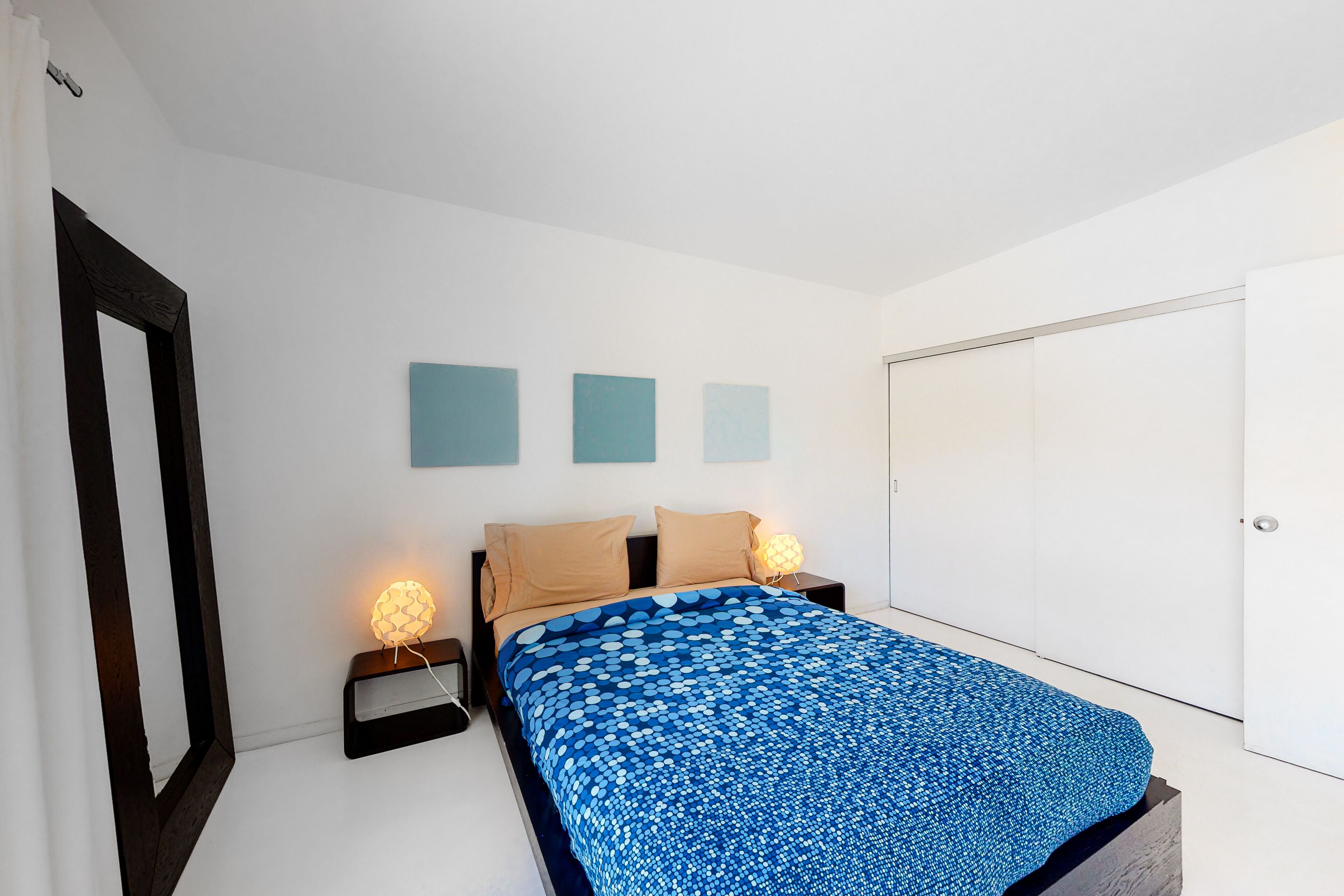 A bedroom with a bed, two bedside tables, a nightstand, and a wardrobe.