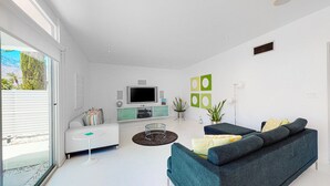A modern living room with a sofa, TV, and a small table. - Elegant Wexler home with private outdoor pool & spa - 2 dogs welcome (Palm Springs)