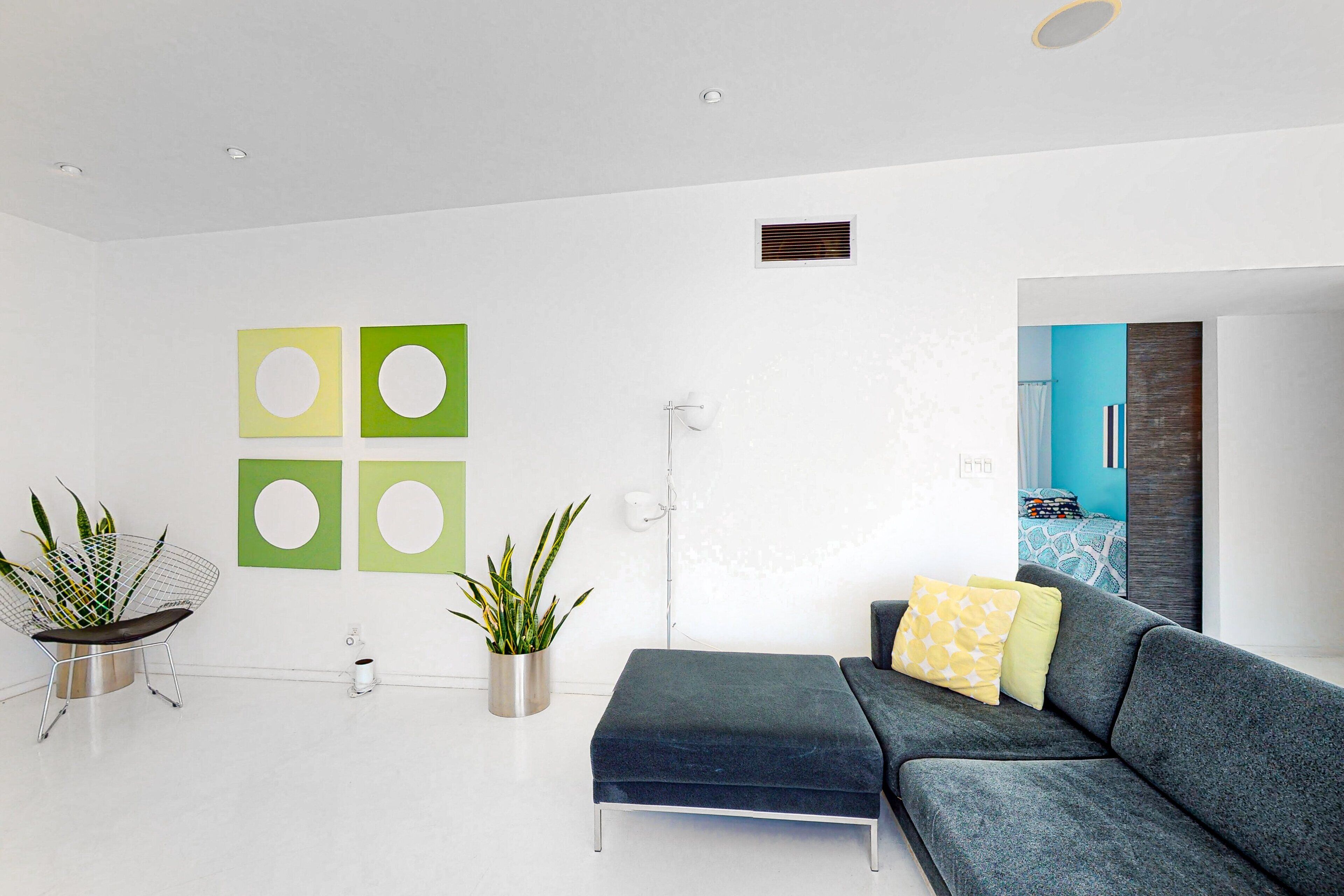 Een moderne woonkamer met een hoekbank, twee potplanten en een wandlamp.