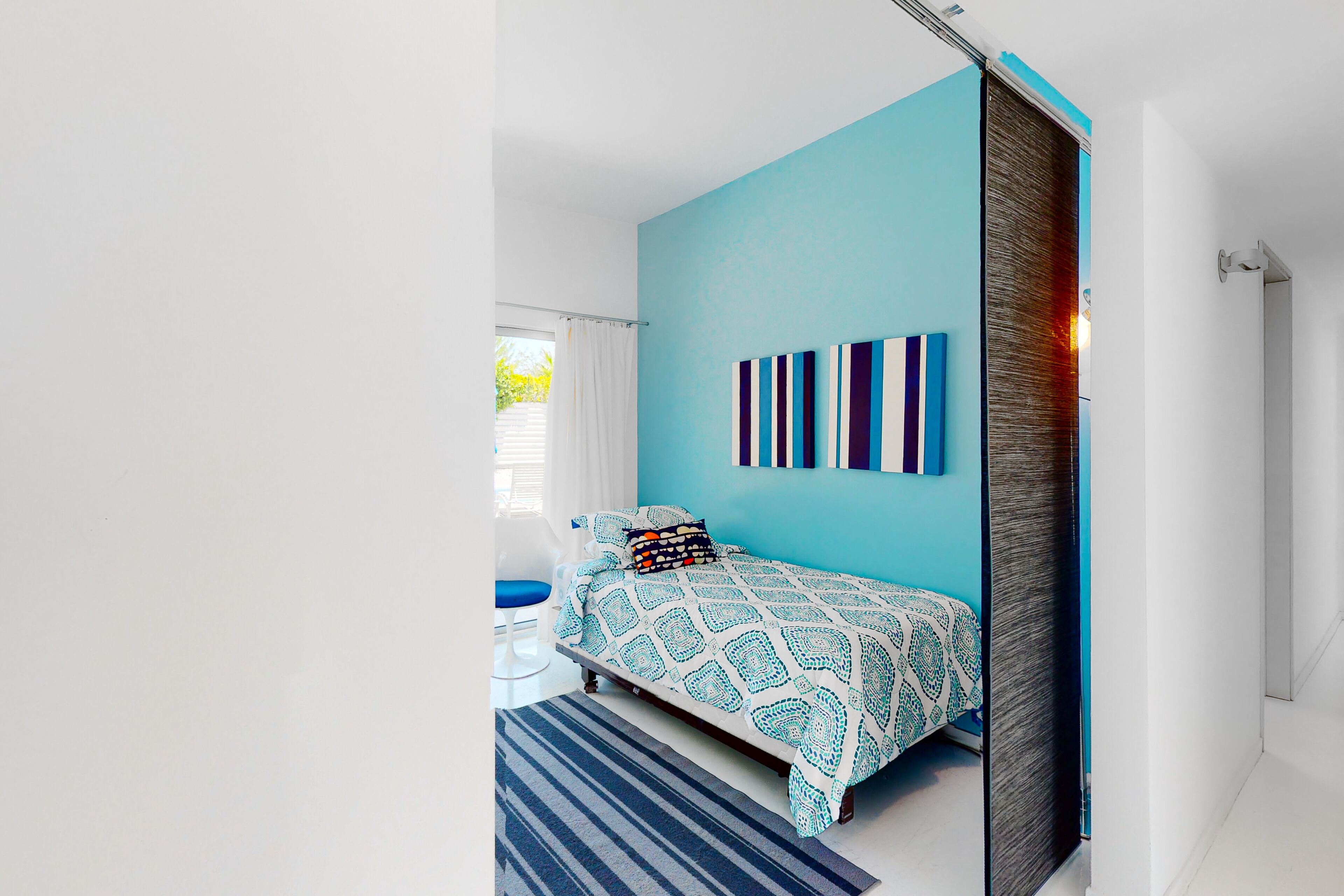 Une chambre à coucher moderne avec un lit, un mur d’accent bleu et une vue sur l’extérieur.