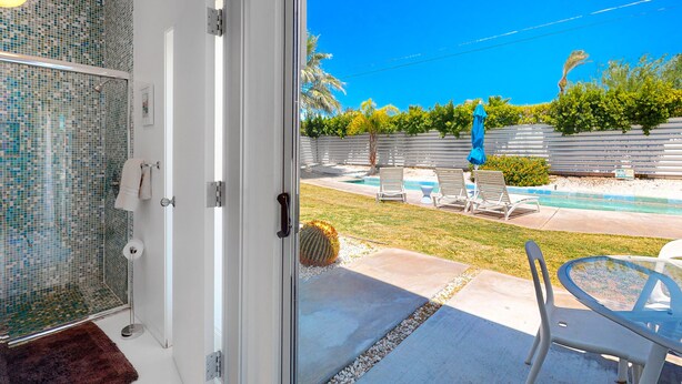 A glass door leading to a patio with a pool, lounge chairs, and a cactus. - Elegant Wexler home with private outdoor pool & spa - 2 dogs welcome (Palm Springs)