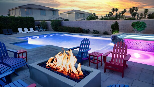 Piscina con una chimenea, sillas de descanso y vista a casas al atardecer.
