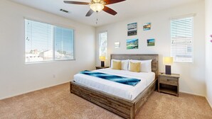 Un dormitorio con cama, ventilador de techo, mesita de noche y ventana con persianas.