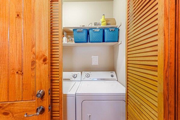 A laundry room with two washing machines, a shelf with blue baskets, and a wooden door.
