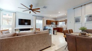 A modern living room with a sofa, TV, ceiling fan, and dining area with chairs and a table.