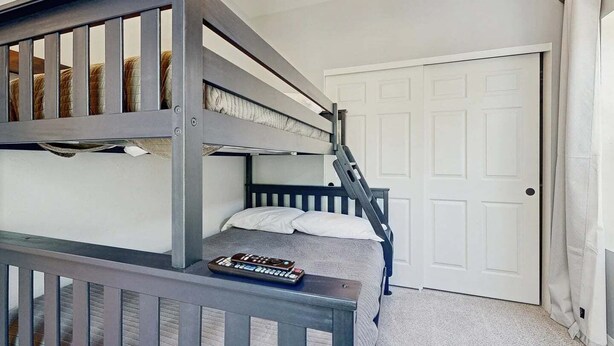 Een slaapkamer met een stapelbed, een ladder, een deur en een afstandsbediening op het bed.
