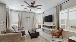 Een moderne woonkamer met een bank, fauteuil, televisie, open haard en plafondventilator.