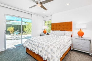 A bedroom with a large bed, a ceiling fan, a nightstand, and a view of the outdoors through a sliding glass door. - Bright mid-century modern home w/ private pool and spa, gas grill, dogs welcome (Palm Springs)